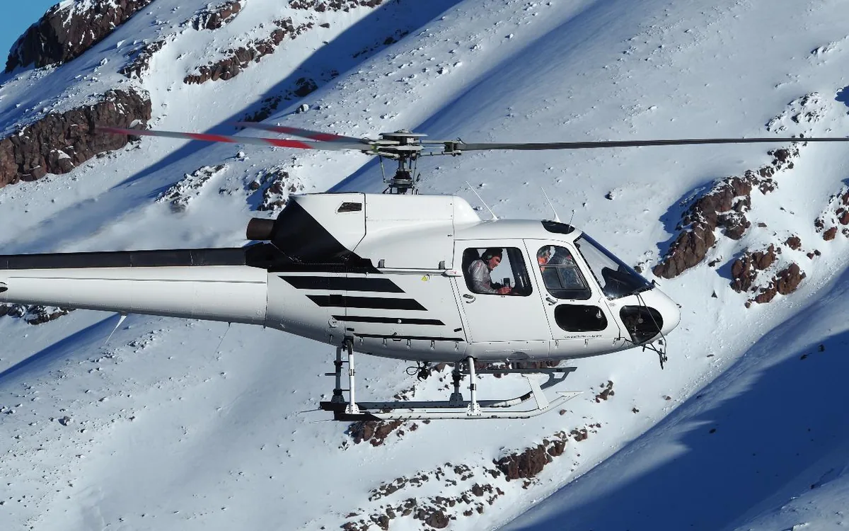 A helicopter hovering beside a snow-covered rocky slope