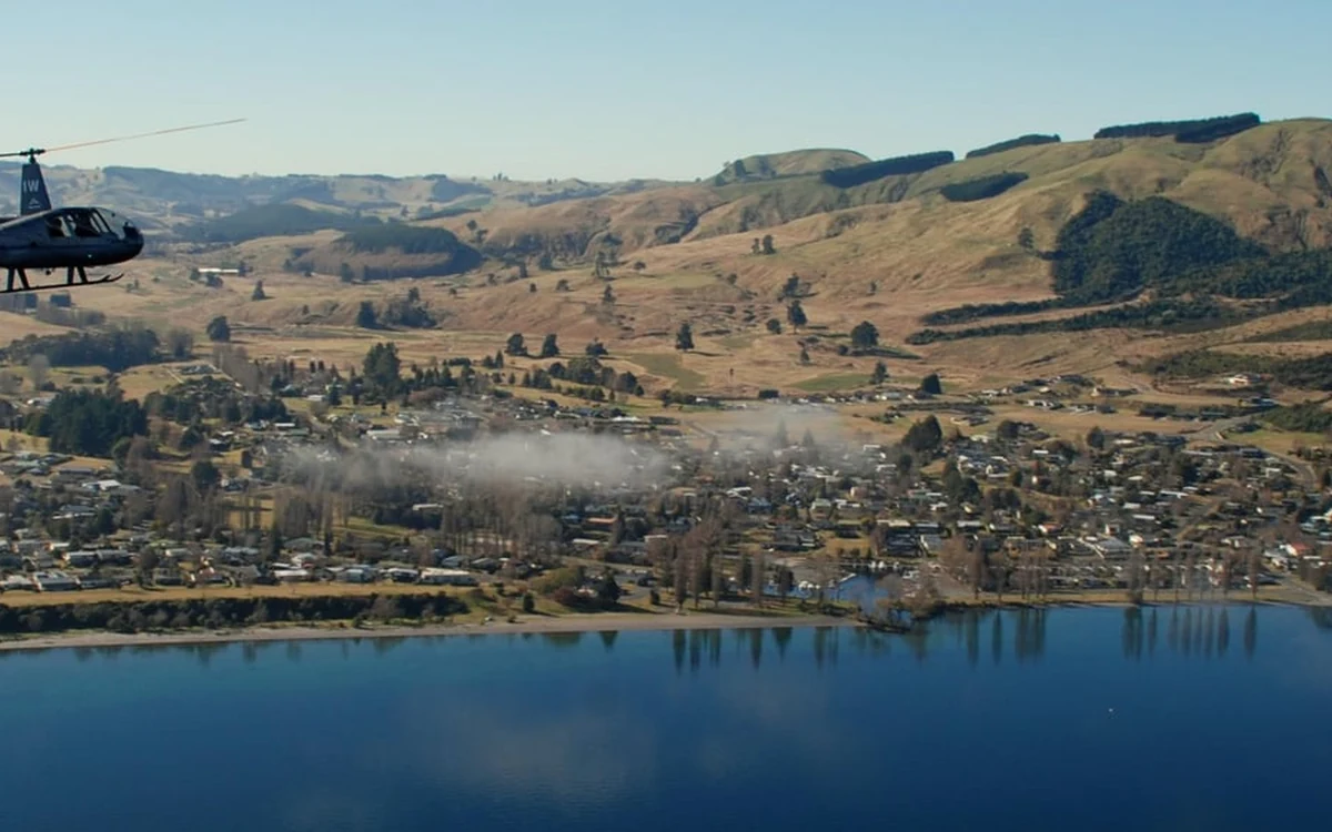A helicopter flying above Taupo township with the lake below and farmland behind