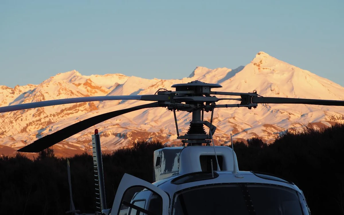 A helicopter parked below a snow-covered volcano lit by low sun