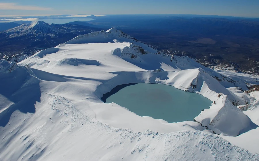 Snowy volcanic peaks on the horizon beyond the shore of Lake Taupo